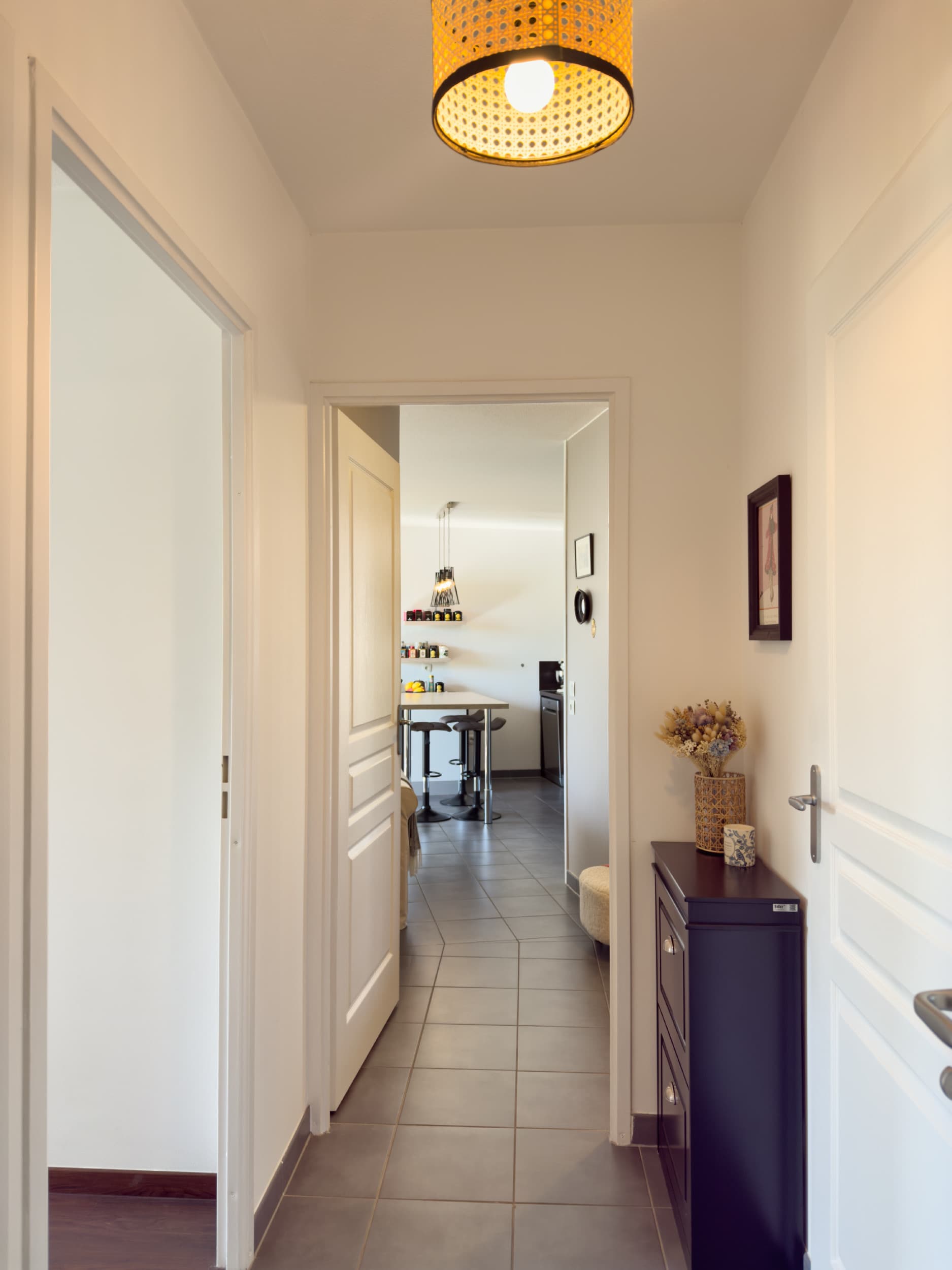 Couloir cadré sur l'enfilade vers la cuisine, suspension en rotin tressé